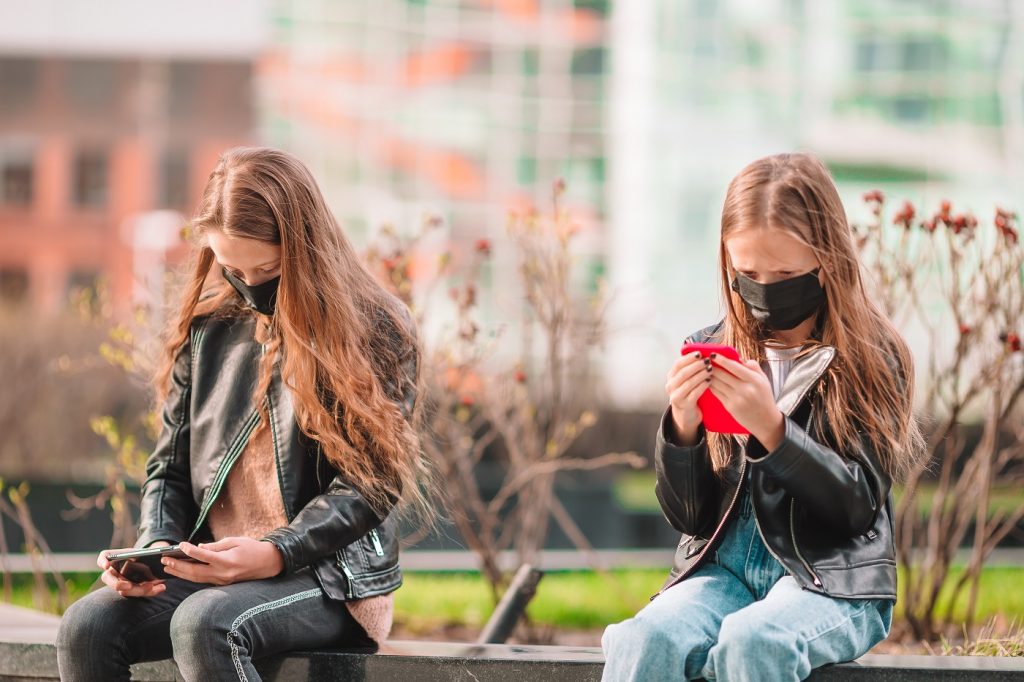 Little girl wearing a mask outdoors for prevent virus and playing smartphone. Protection against Coronavirus and gripp